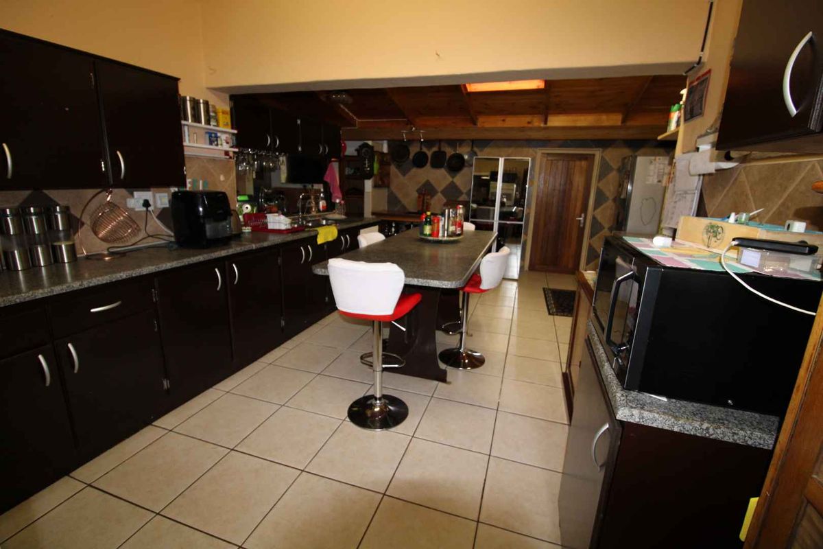 Spacious kitchen featuring dark cabinetry, granite-look countertops, a central breakfast island, and tiled flooring with an exposed timber ceiling beam.
