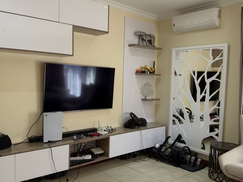 A well-maintained living room featuring custom built-in cabinetry, wall-mounted shelving, and a split-system air conditioning unit.