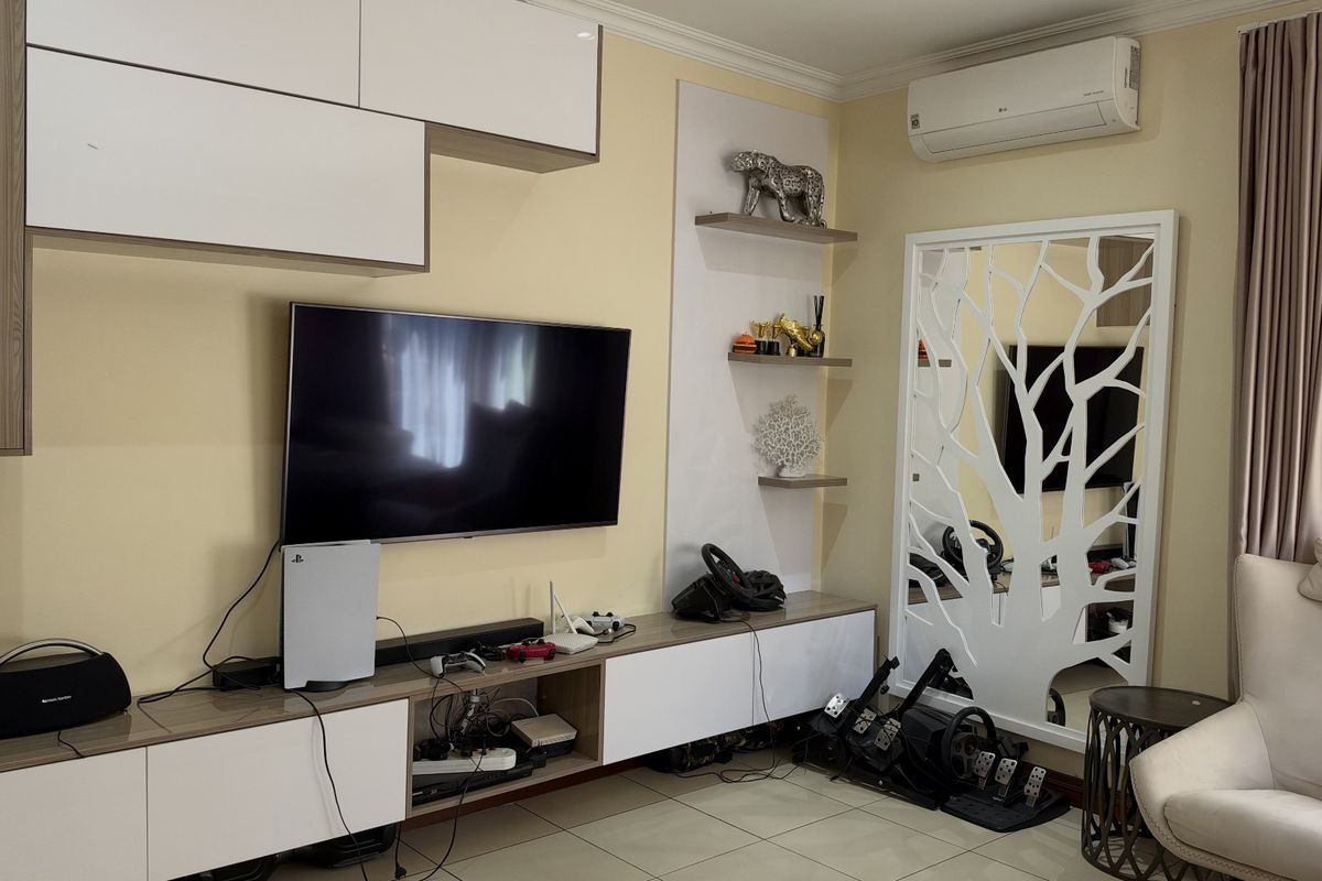 A well-maintained living room featuring custom built-in cabinetry, wall-mounted shelving, and a split-system air conditioning unit.