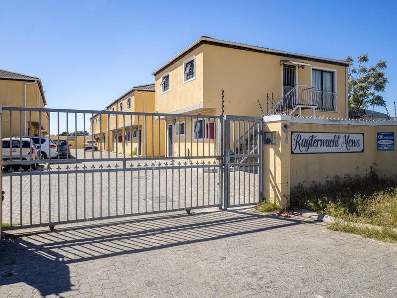 Front entrance view of Ruijterwacht Mews apartment complex, featuring a secure gated access point, paved driveway, and multi-story residential units with balconies.