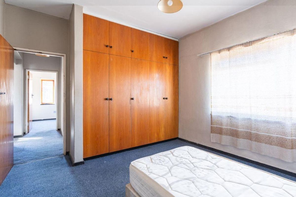 A bedroom featuring built-in wooden wardrobes, carpeted flooring, and natural light through a window, with an adjacent hallway visible.