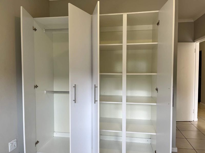 A clean, functional bedroom featuring a large white built-in wardrobe with ample hanging space and shelving, complemented by neutral tiled flooring.