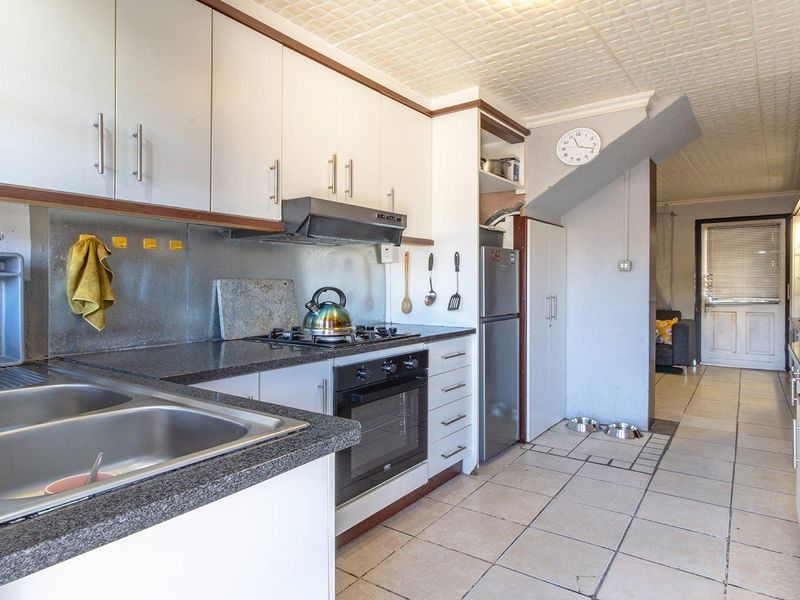 Functional kitchen featuring granite countertops, built-in oven with gas hob, extractor fan, and ample cabinetry, leading into an adjacent living area.