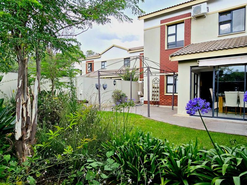Rear view of the townhouse featuring a landscaped garden, paved patio area, and large sliding glass doors providing access to the interior living space.