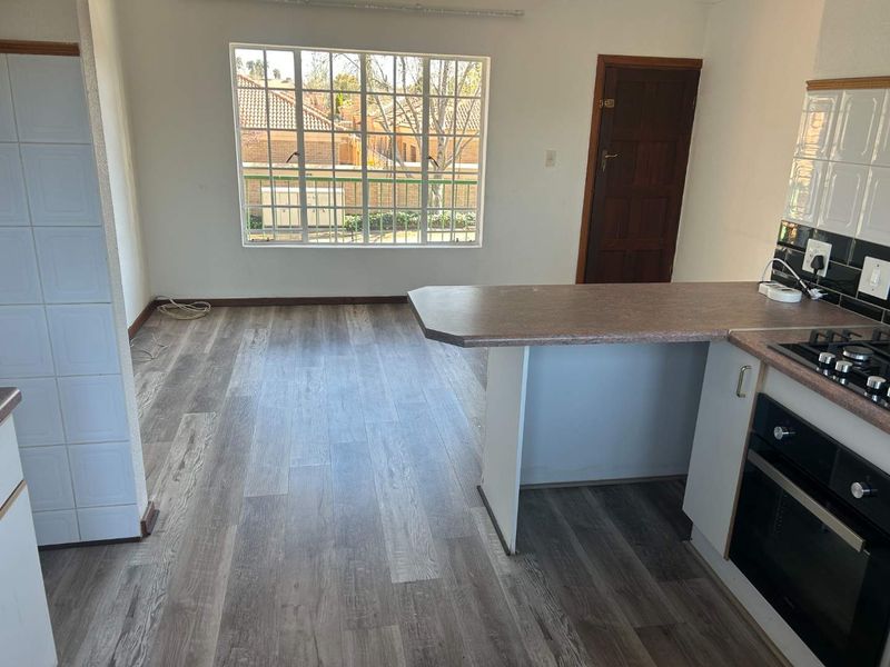 An open-plan kitchen and living area featuring modern laminate flooring, a built-in oven, gas hob, and a breakfast bar, offering a blank canvas for customization.
