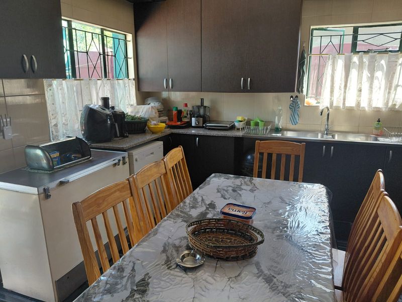 A functional kitchen featuring dark wood cabinetry, laminate countertops, and a stainless steel sink, with security bars installed on the windows.