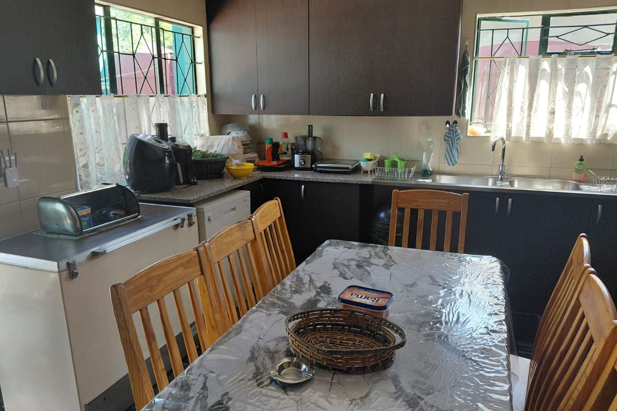 A functional kitchen featuring dark wood cabinetry, laminate countertops, and a stainless steel sink, with security bars installed on the windows.