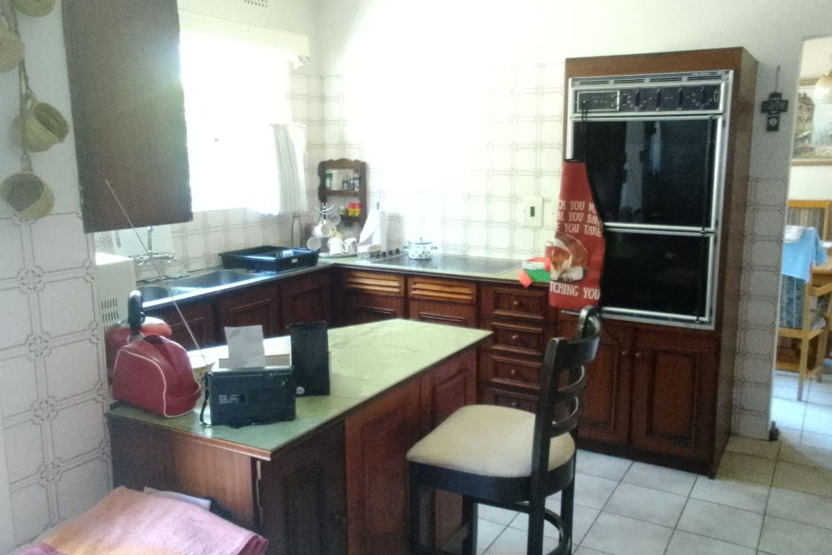 A dated kitchen featuring traditional wooden cabinetry, a built-in double oven, tiled backsplash, and a central island with a breakfast bar.