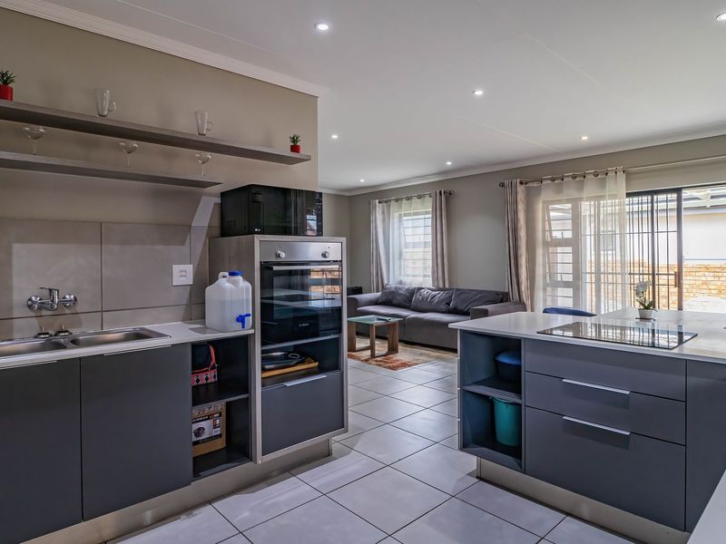 Modern open-plan kitchen and living area featuring sleek cabinetry, a central island with a hob, built-in oven, and tiled flooring throughout.