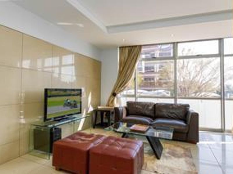 A bright living room featuring a large tiled feature wall, recessed ceiling lighting, and expansive floor-to-ceiling windows providing ample natural light.