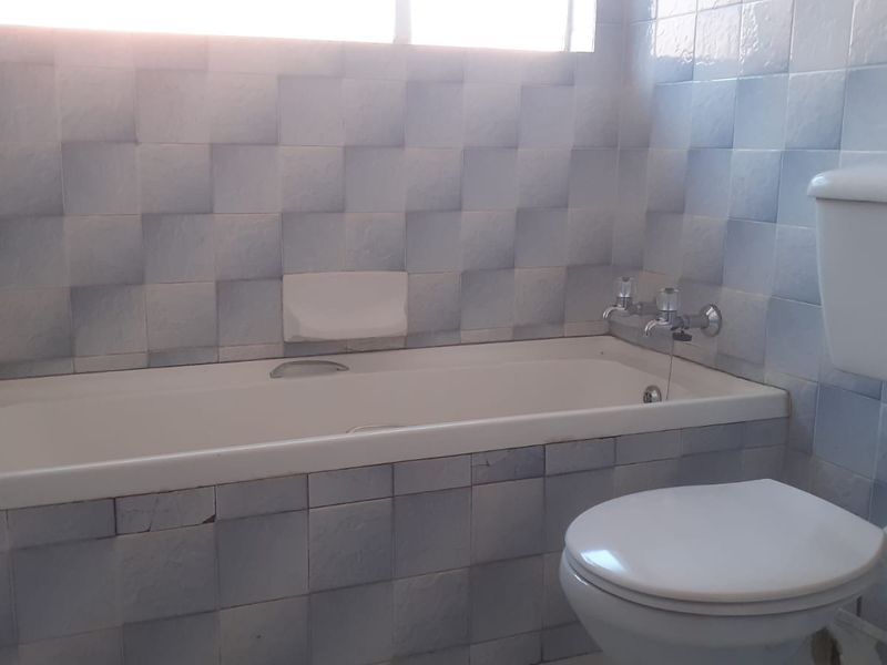 A dated bathroom featuring a standard bathtub, toilet, and blue wall tiling, requiring cosmetic updates to modernize the space.