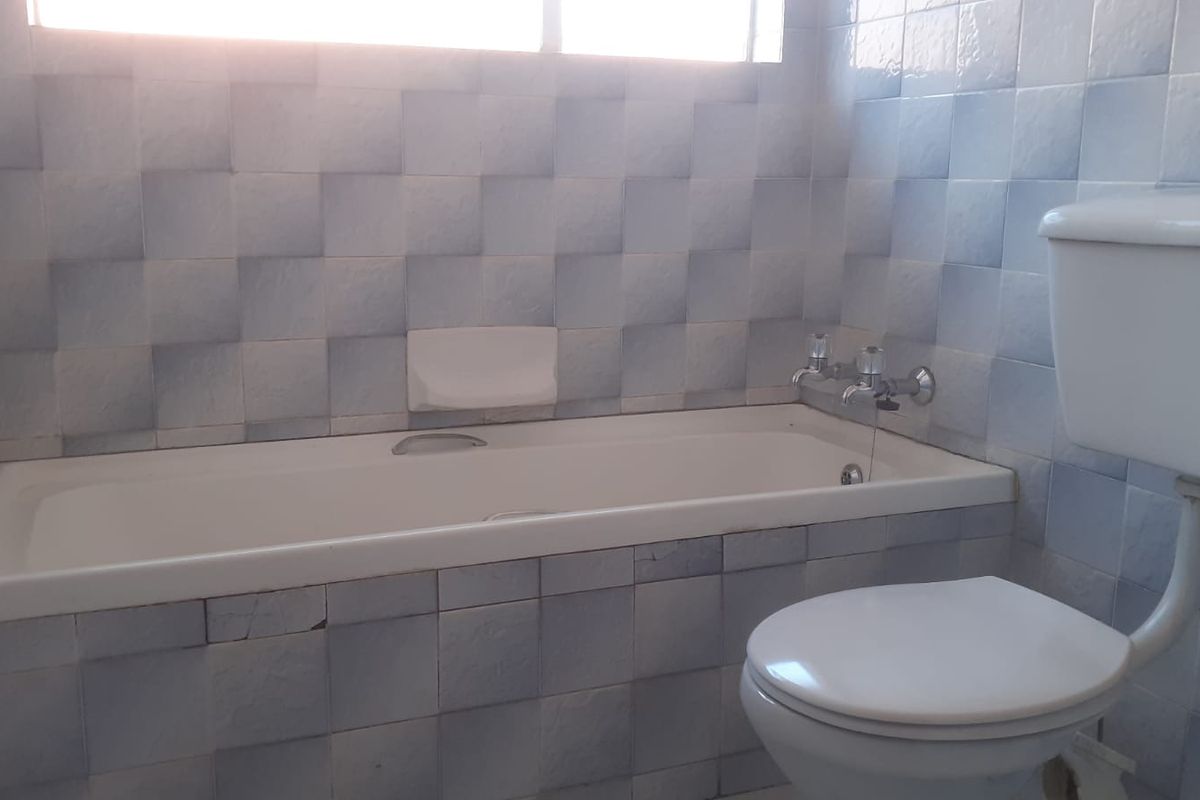 A dated bathroom featuring a standard bathtub, toilet, and blue wall tiling, requiring cosmetic updates to modernize the space.