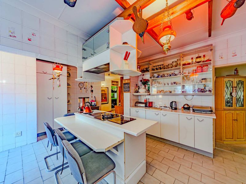 A functional kitchen featuring a central island with integrated cooktop, ample built-in cabinetry, and exposed timber ceiling beams, offering a classic, dated aesthetic.