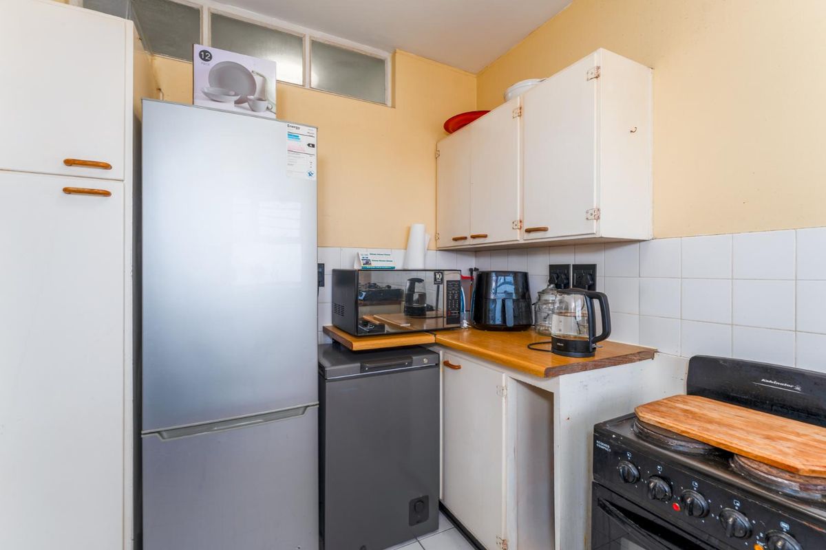 A compact kitchen featuring white cabinetry, tiled splashbacks, and a freestanding stove, offering a functional layout with potential for modernization.