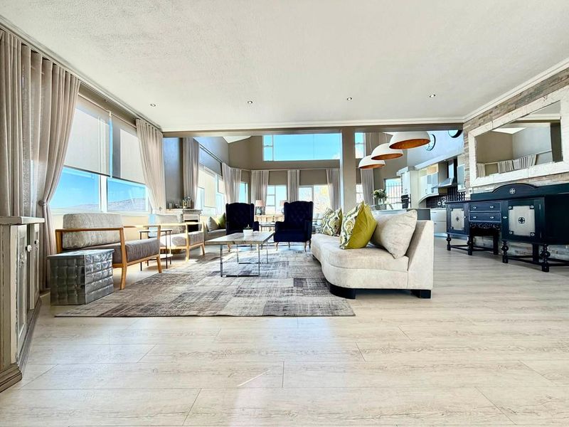 Spacious open-plan living area featuring light laminate flooring, recessed lighting, and a seamless flow into the modern kitchen with a stone feature wall.