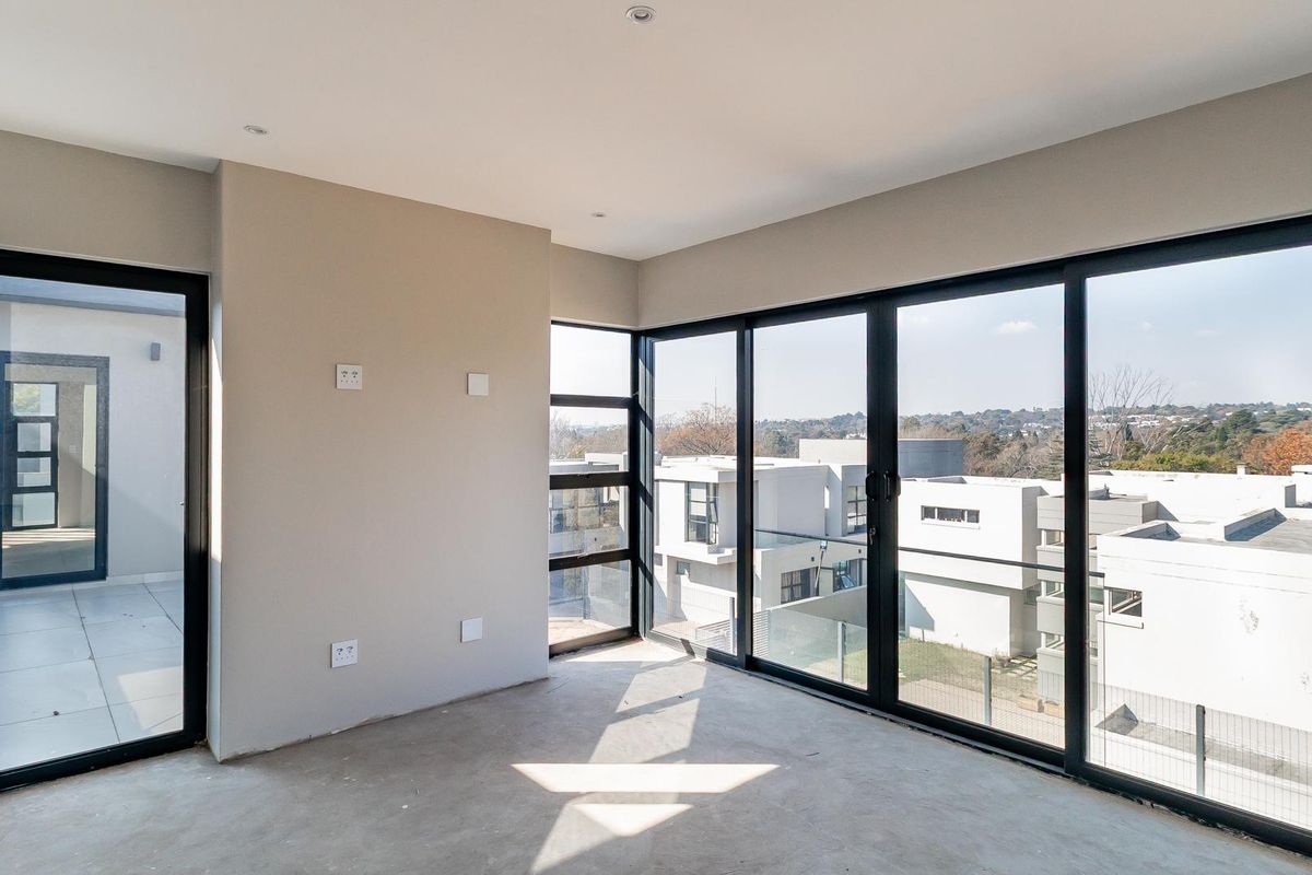 A bright, empty living area featuring modern black aluminium sliding doors, recessed lighting, and expansive views of the surrounding estate.
