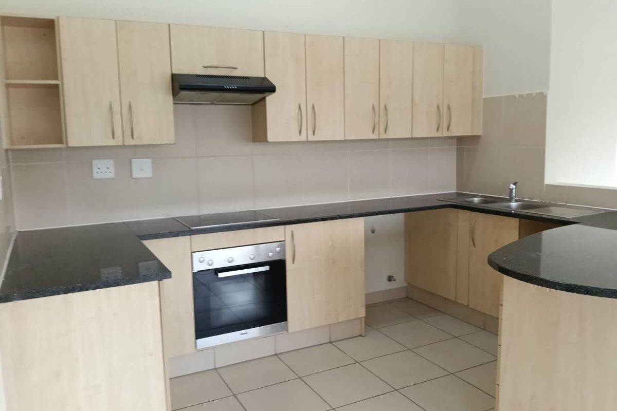 A functional kitchen featuring light wood cabinetry, granite countertops, built-in oven and hob, and tiled flooring. The space is clean and ready for use.