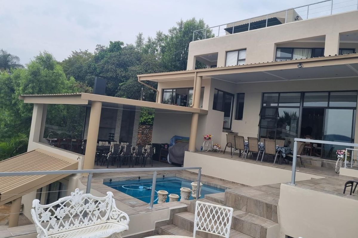 A multi-level rear exterior featuring a swimming pool, covered patio area, and tiled terrace with glass balustrades, ideal for outdoor entertaining.