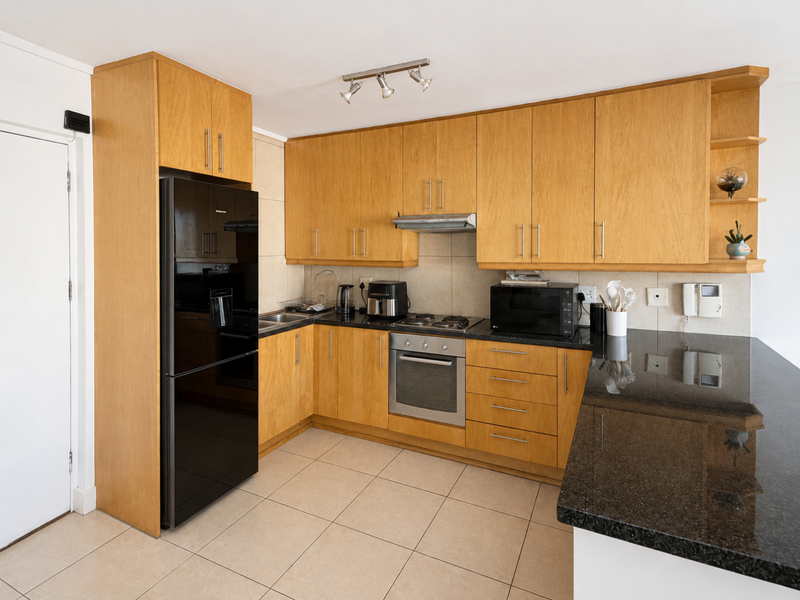 A functional kitchen featuring light wood cabinetry, dark granite countertops, built-in oven, electric hob, and tiled flooring.