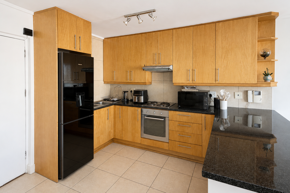 A functional kitchen featuring light wood cabinetry, dark granite countertops, built-in oven, electric hob, and tiled flooring.