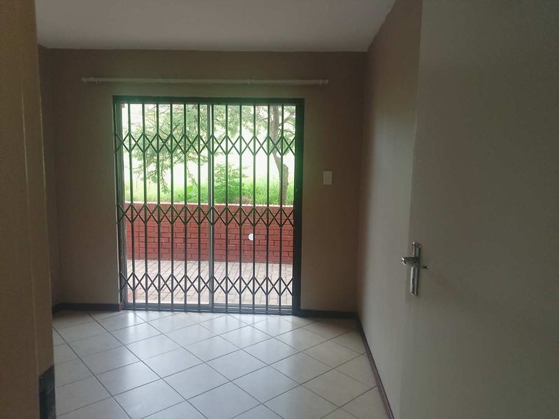 An empty living room featuring tiled flooring and a sliding glass door with a security gate, providing access to an outdoor patio area.