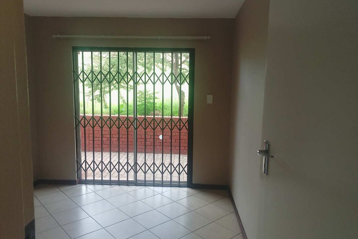 An empty living room featuring tiled flooring and a sliding glass door with a security gate, providing access to an outdoor patio area.