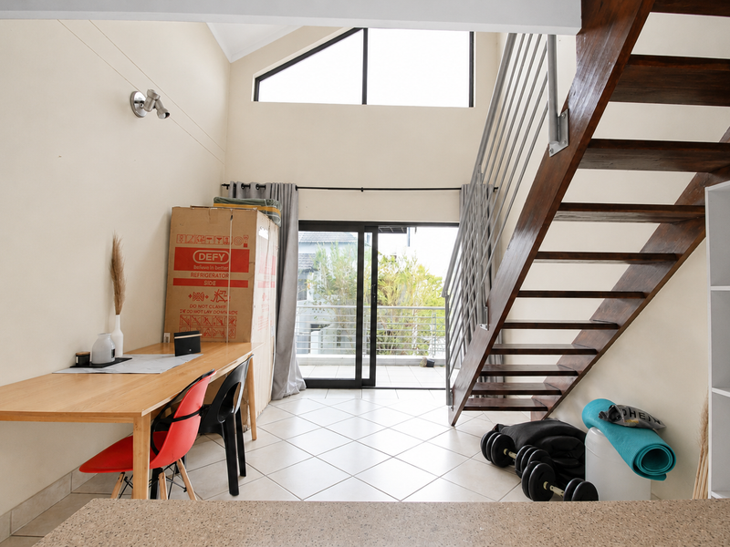 Open-plan living area featuring a timber staircase, vaulted ceilings with high-level windows, and direct access to a balcony through sliding glass doors.