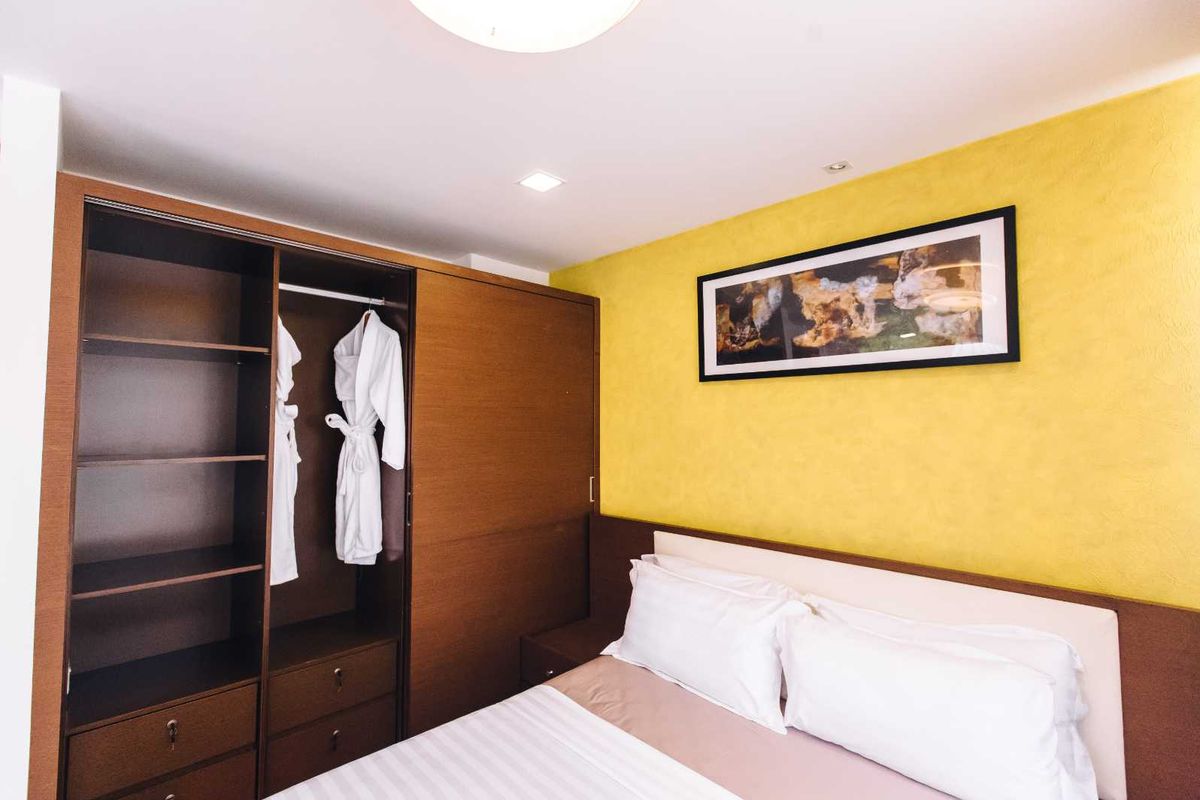 A well-maintained bedroom featuring a built-in wooden wardrobe with shelving and hanging space, complemented by a vibrant yellow accent wall.
