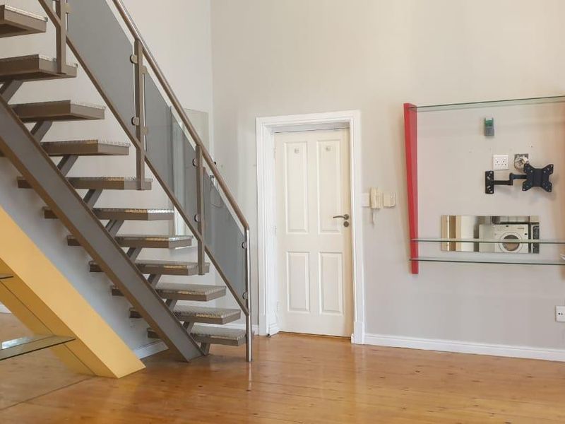 Open plan living area featuring a modern metal and glass staircase, hardwood flooring, and a built-in wall-mounted shelving unit.