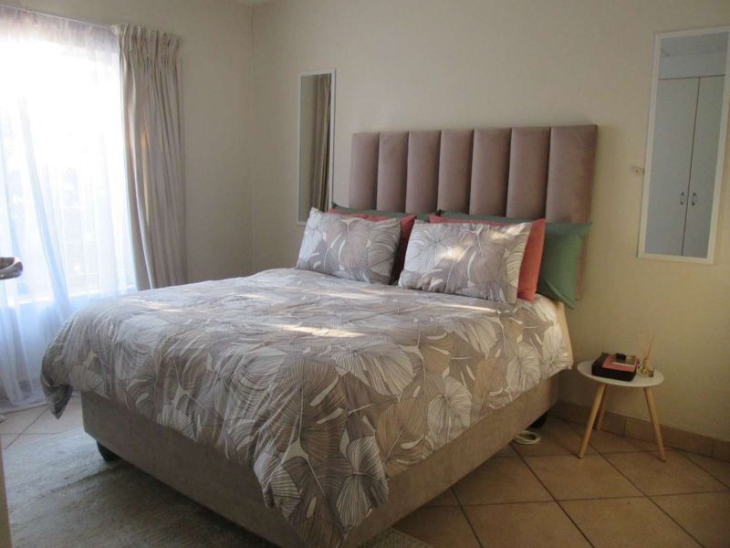 A well-lit bedroom featuring tiled flooring and a built-in wall mirror, providing a comfortable and functional living space.