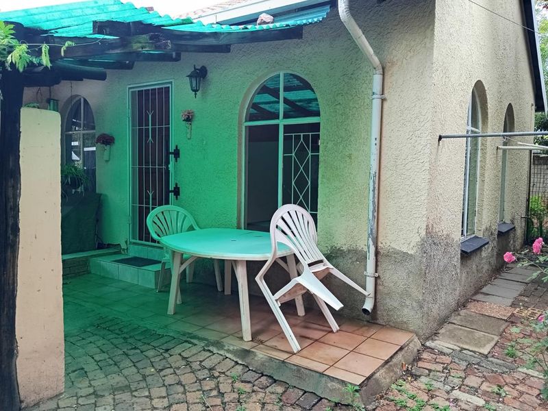 A covered patio area featuring arched windows, tiled flooring, and a pergola structure, offering a functional outdoor space for relaxation.