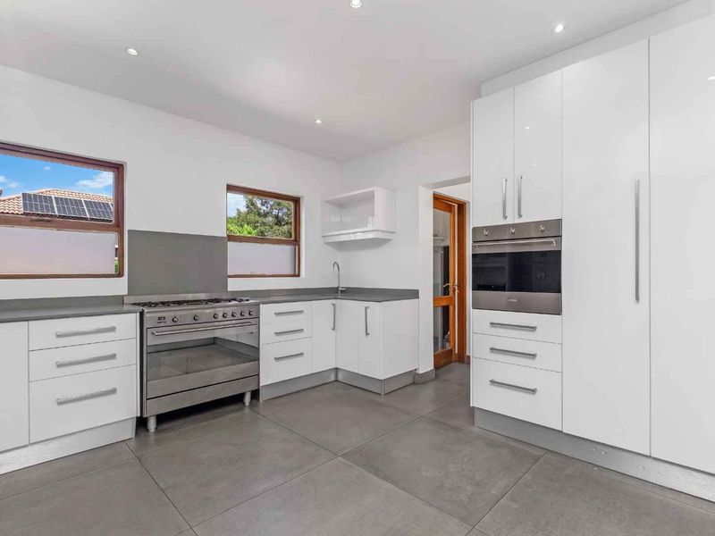 Modern kitchen featuring white high-gloss cabinetry, stone countertops, stainless steel appliances, and large format floor tiles.