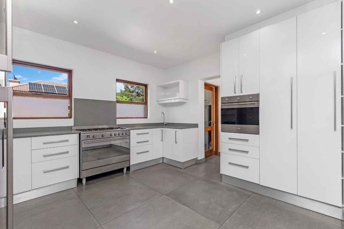Modern kitchen featuring white high-gloss cabinetry, stone countertops, stainless steel appliances, and large format floor tiles.