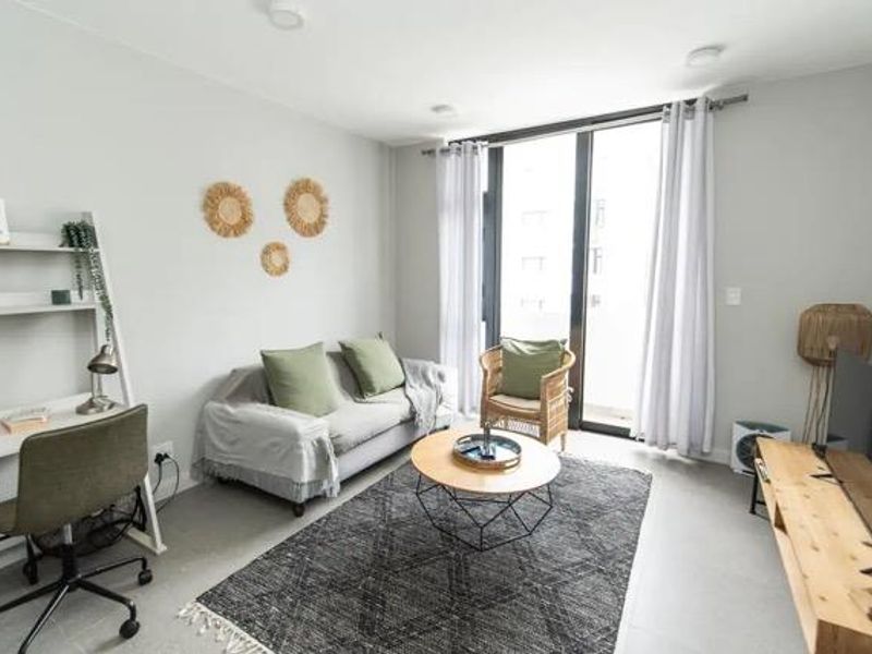 A bright and modern living room featuring tiled flooring, recessed lighting, and a large sliding glass door providing access to the balcony.