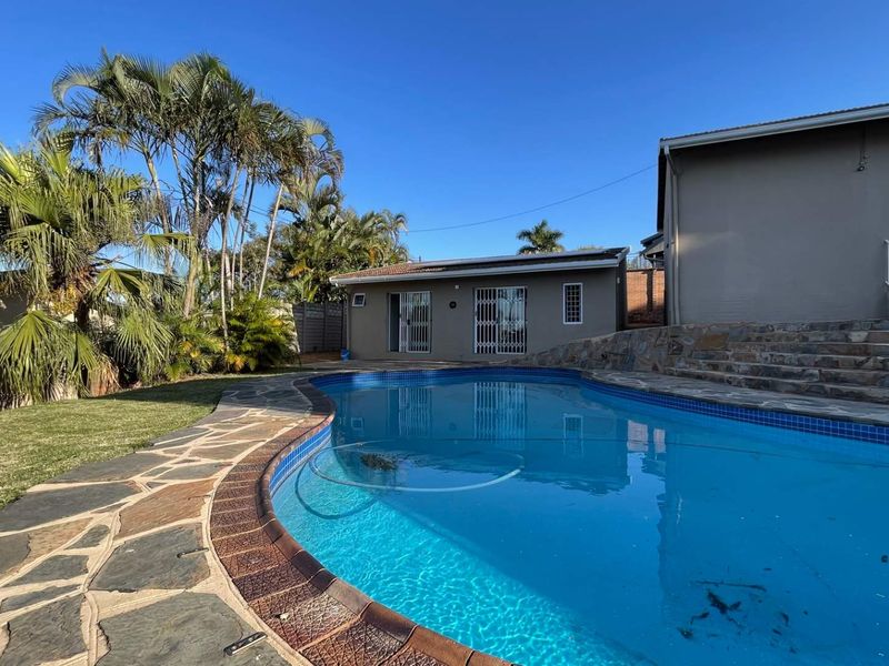 Outdoor pool area featuring stone paving, a retaining wall, and access to the main dwelling and outbuilding with security gates.