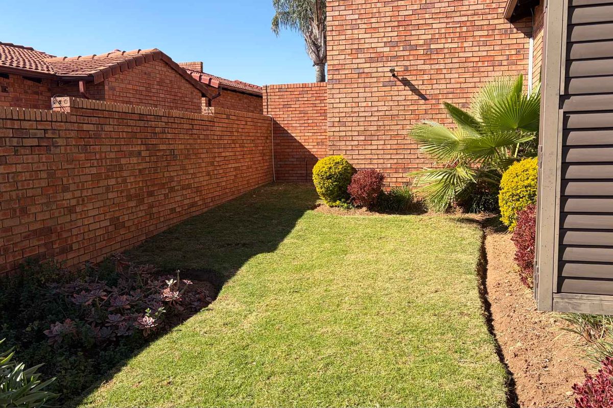 A private rear garden area featuring a well-maintained lawn, established garden beds, and high brick boundary walls for added privacy.