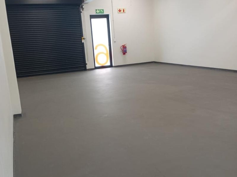 A clean, empty industrial garage space featuring an epoxy floor, roller shutter door, and exposed overhead cable tray infrastructure.