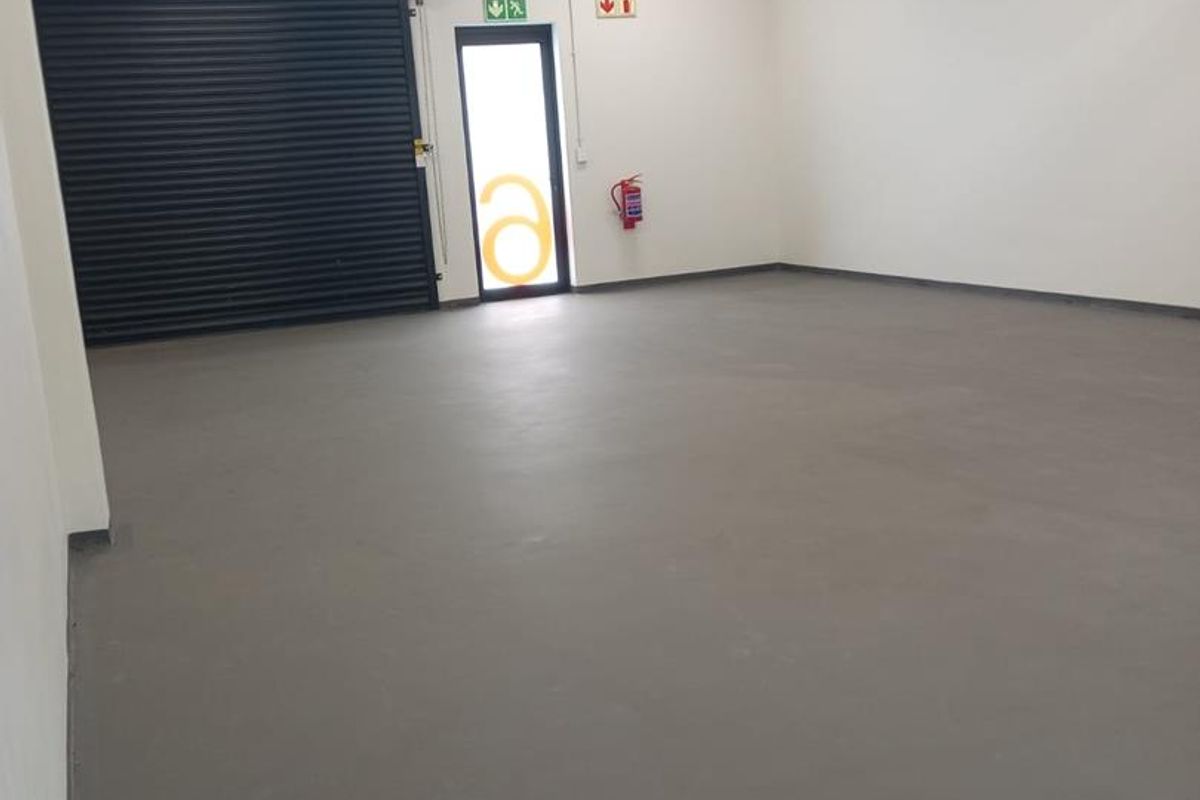 A clean, empty industrial garage space featuring an epoxy floor, roller shutter door, and exposed overhead cable tray infrastructure.