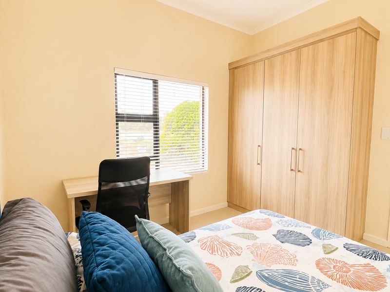 A well-maintained bedroom featuring light-toned built-in wardrobes, tiled flooring, and a window with fitted venetian blinds.