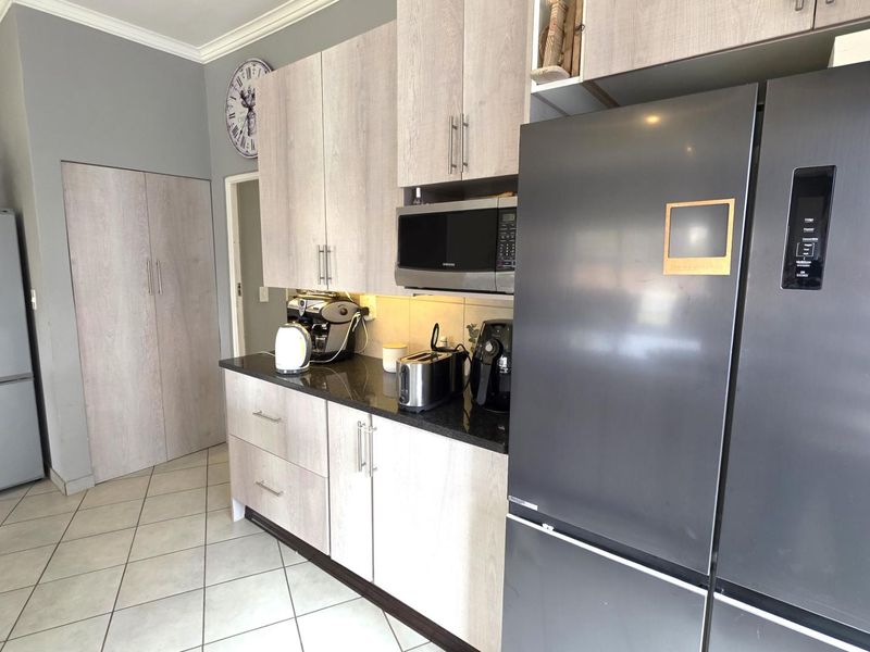 A functional kitchen featuring light wood-grain cabinetry, dark granite countertops, built-in microwave, and tiled flooring.