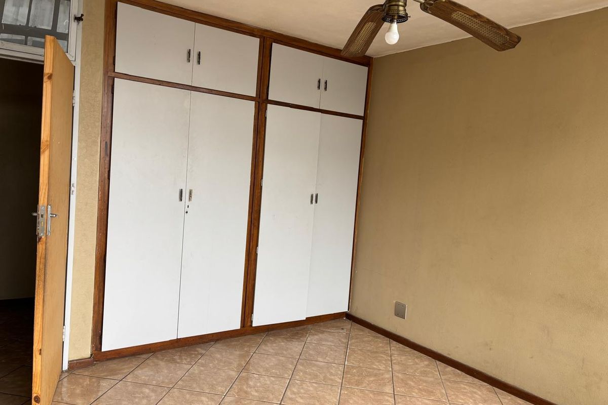 A bedroom featuring built-in cupboards with white doors, tiled flooring, and a ceiling fan.