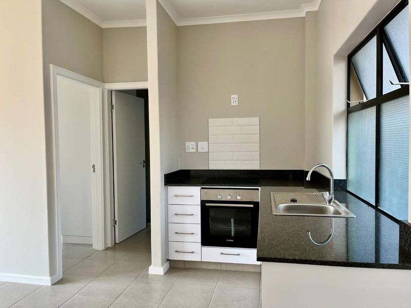 A clean, modern kitchen featuring granite countertops, a built-in oven with hob, subway tile backsplash, and neutral tiled flooring.