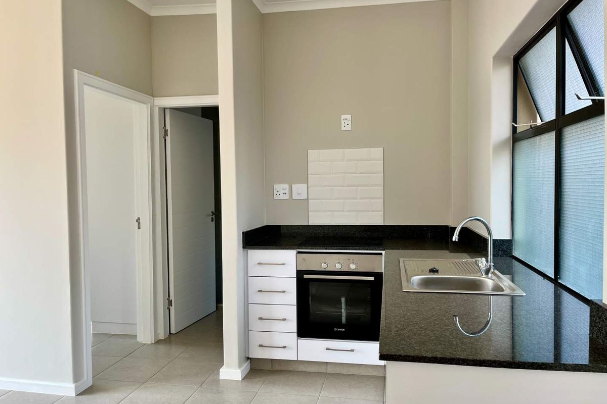 A clean, modern kitchen featuring granite countertops, a built-in oven with hob, subway tile backsplash, and neutral tiled flooring.