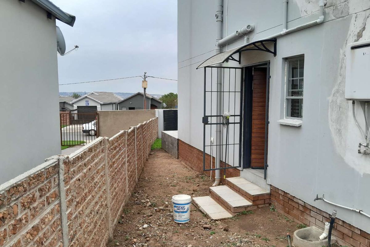 Side exterior view of the property featuring a security gate, tiled entrance step, and exposed ground area along the boundary wall.
