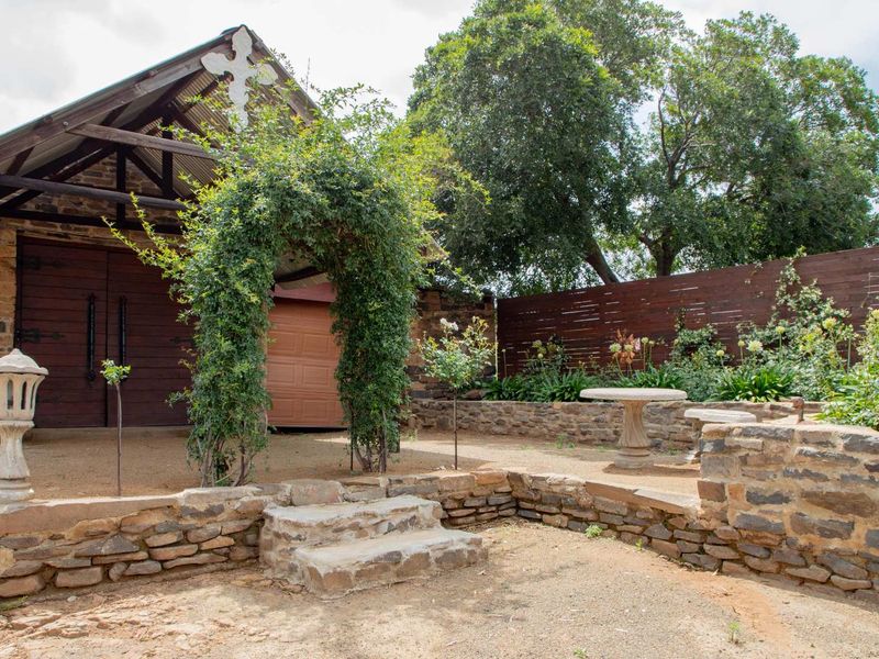 A charming rustic outdoor area featuring stone retaining walls, stone steps, and a barn-style structure with timber doors and a corrugated metal roof.