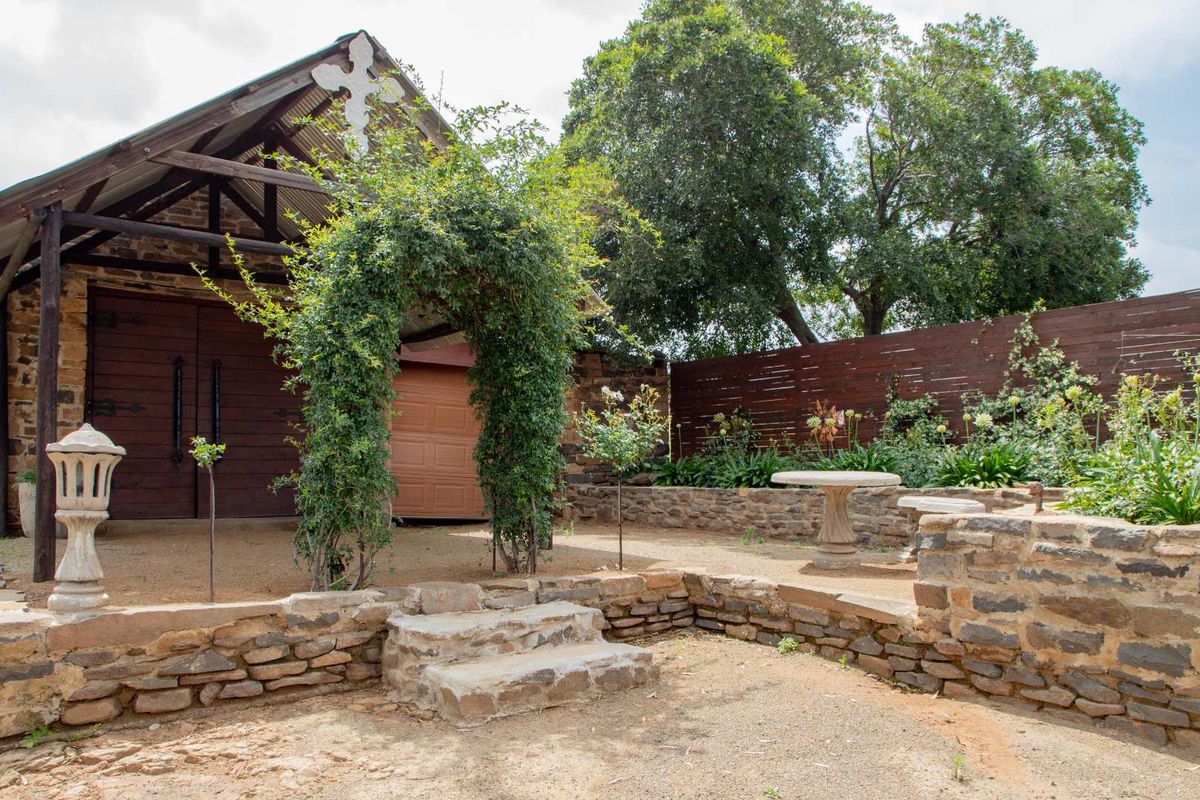 A charming rustic outdoor area featuring stone retaining walls, stone steps, and a barn-style structure with timber doors and a corrugated metal roof.