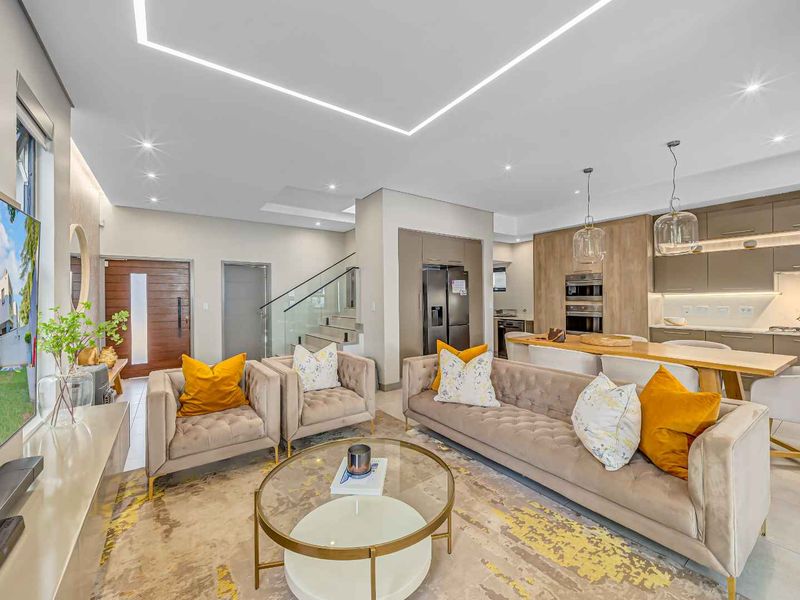 Modern open-plan living area featuring a contemporary kitchen with built-in appliances, sleek cabinetry, recessed ceiling lighting, and a glass-railed staircase.