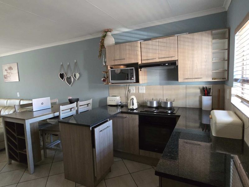 Open-plan kitchen and dining area featuring modern wood-finish cabinetry, granite countertops, integrated appliances, and tiled flooring.
