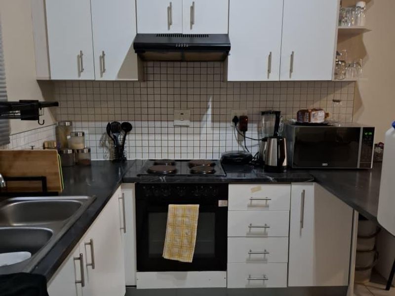 Compact kitchen featuring white cabinetry, dark laminate countertops, tiled backsplash, and integrated oven with hob and extractor fan.