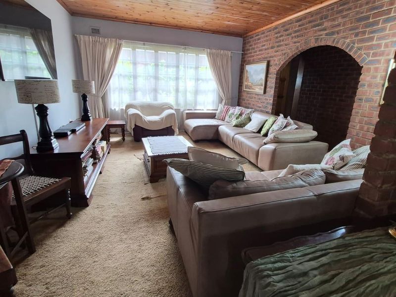 Spacious living room featuring a rustic exposed brick wall, a warm timber-paneled ceiling, and a distinctive brick archway leading to adjacent areas.